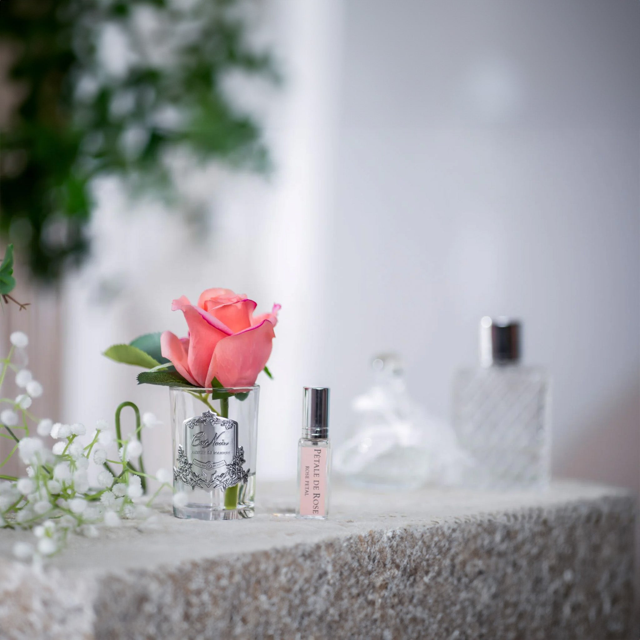 a pink rose in a glass vase next to a bottle of fragrance on a table