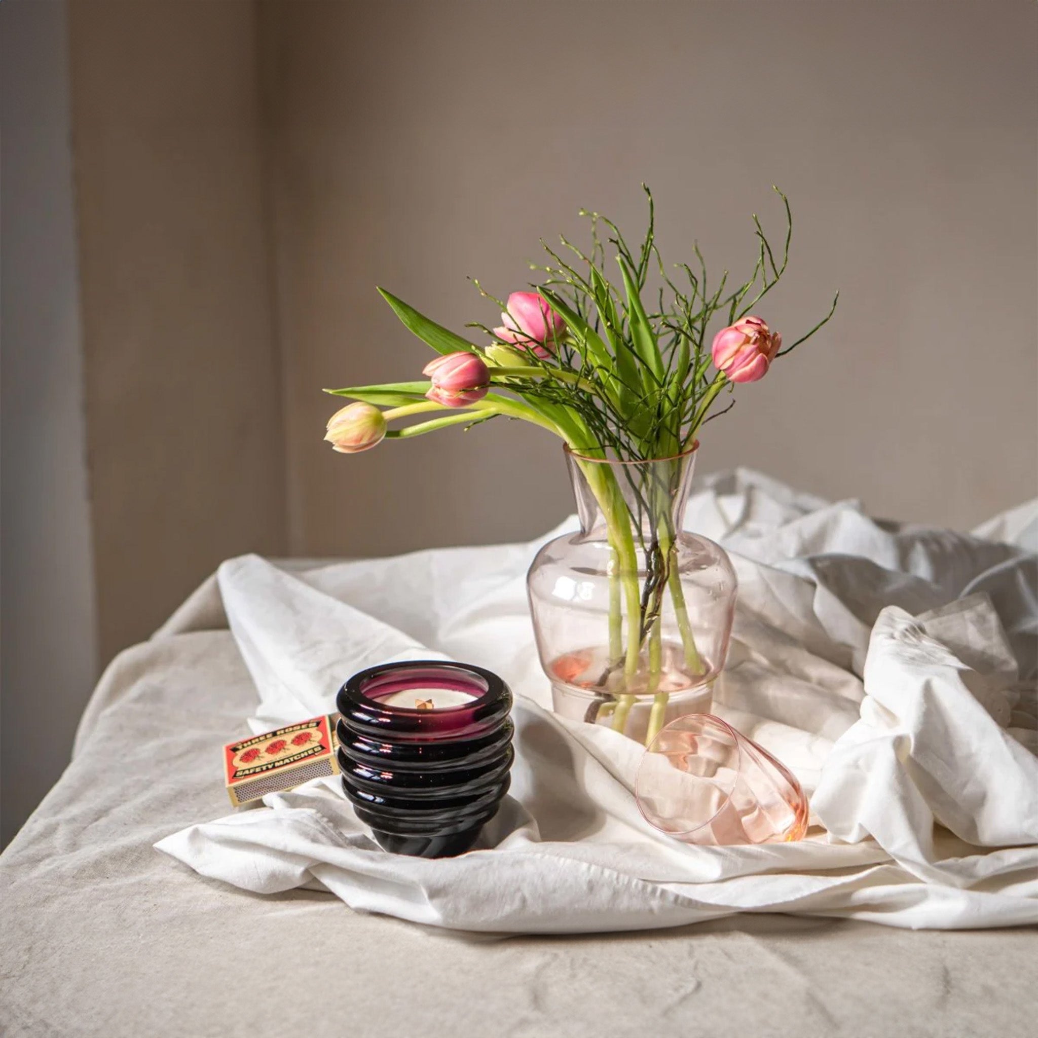 a vase with flowers with a candle and a pink glass on a table