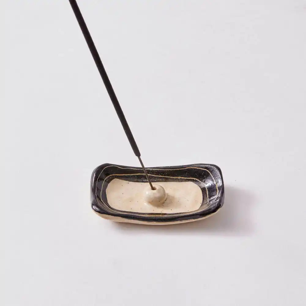 A small black and white incense holder with an incense stick on a white surface