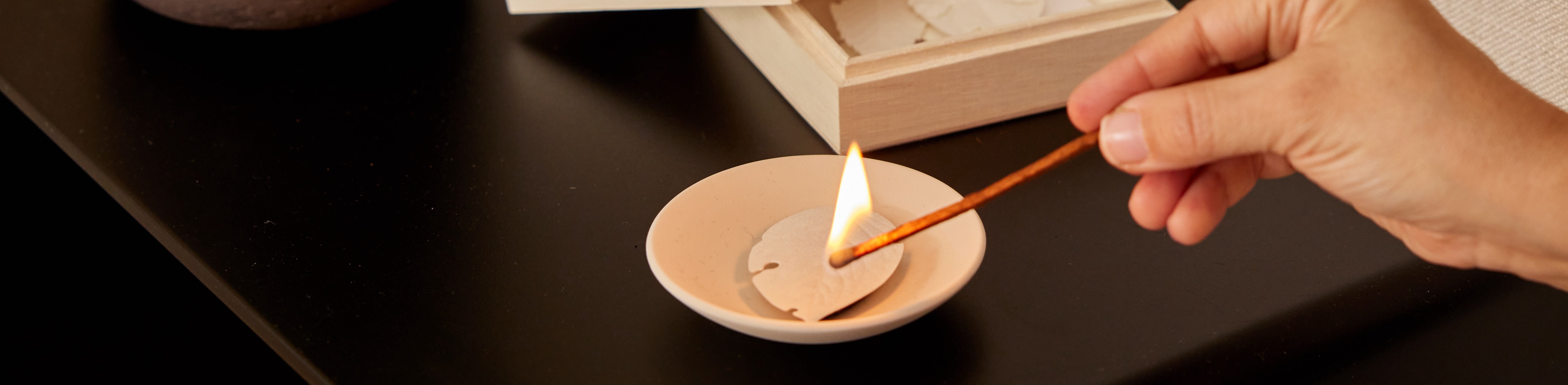 a person lighting a leaf incense in a small bowl