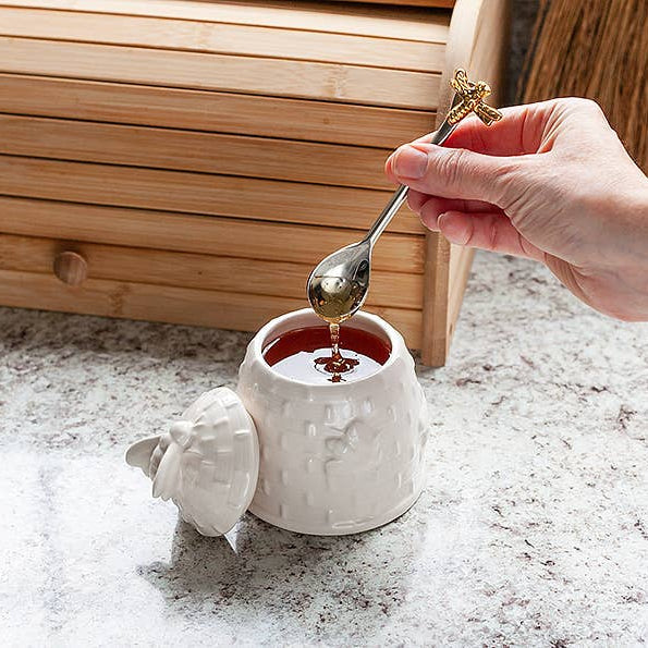 Hand pouring syrup from a spoon into a small white container on a textured surface with wooden background.