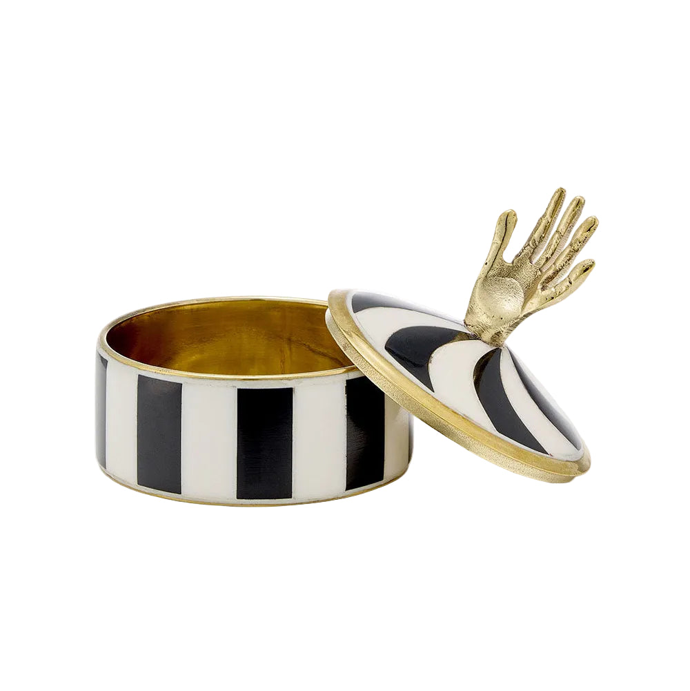 A cylindrical decorative box with black and white vertical stripes, a gold interior, and a gold-toned lid featuring a sculpted hand motif on top, photographed on a clean off-white background.