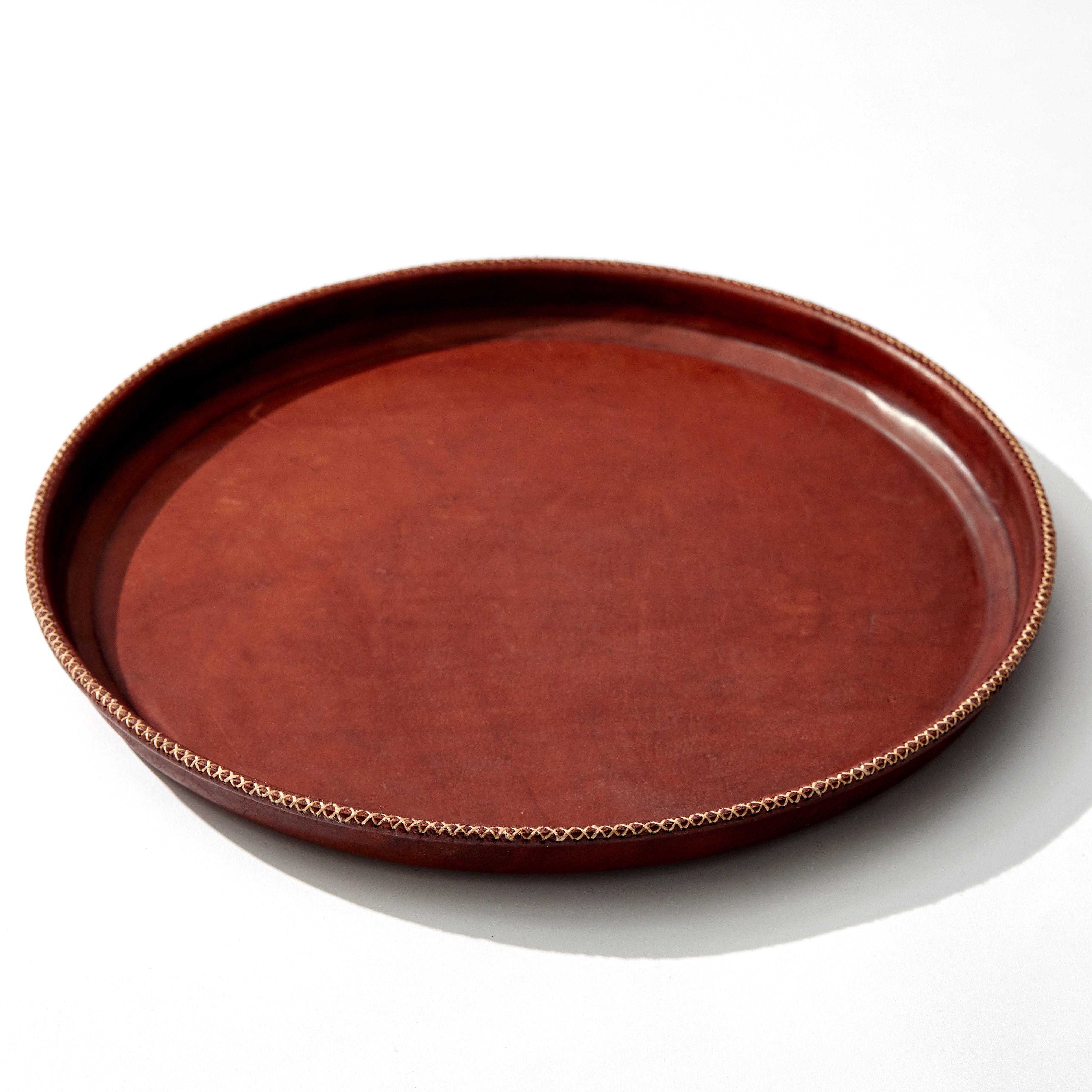 Large Brown Circular Leather Tray with White Hand Stitched Detailing. Angled Shot Of Tray.