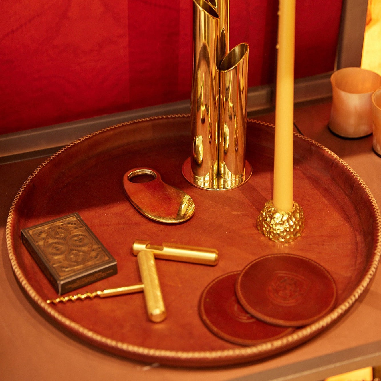 Large Brown Leather Tray with Hand Stitched Detailing Holding our Brass Home Decor Vase and Candleholder Along With A Deck of Cards and Bottle Openers. 