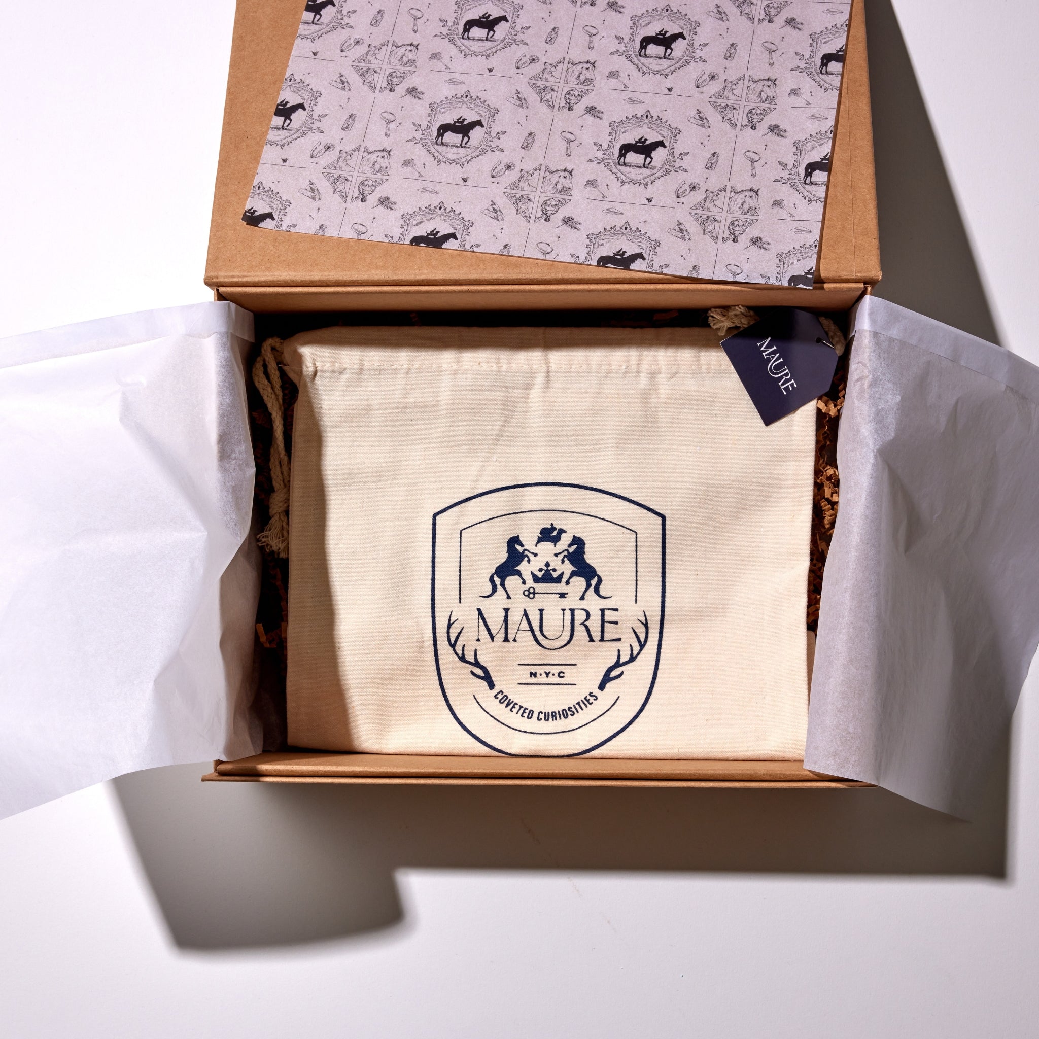Maure gift box packaging includes a traditional equestrian crest pattern tissue paper and dust bag inside of a magnetic kraft box.