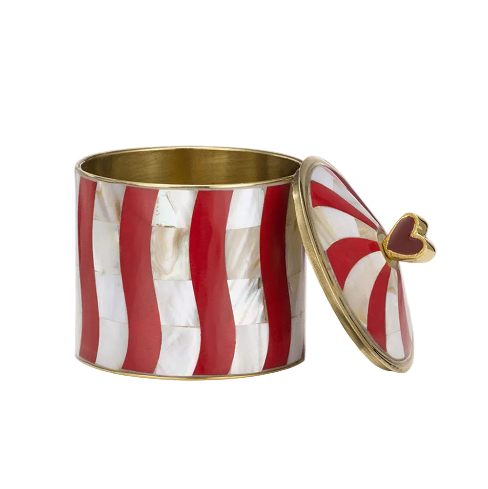 A cylindrical decorative box with a red and white striped pattern made of inlaid mother-of-pearl style panels, featuring a gold-toned metal rim and lid, and a small gold heart accent on the lid.