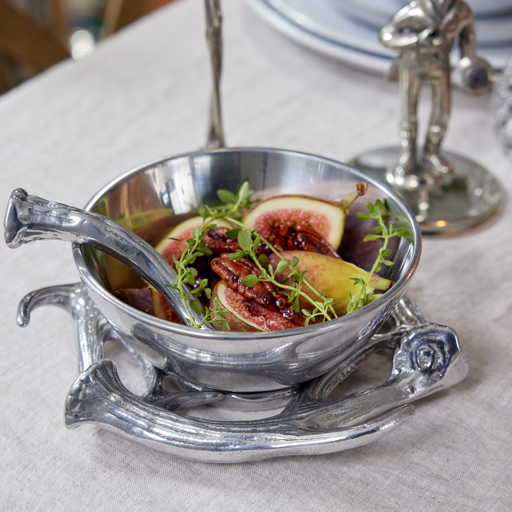 an aluminum serving bowl with antler base and spoon filled with figs