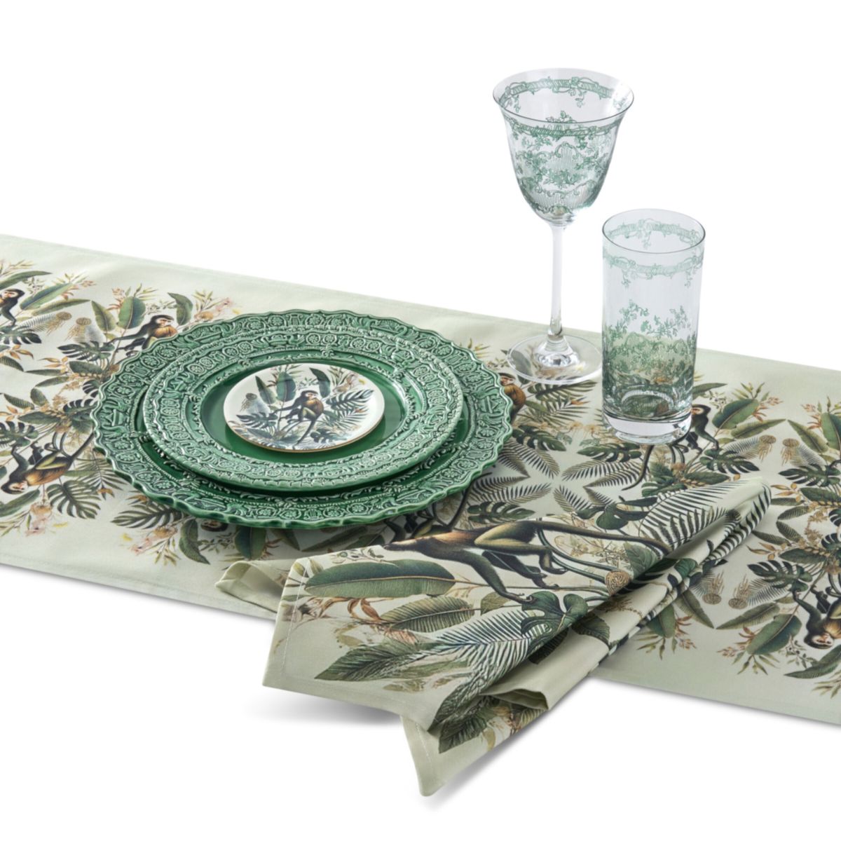 Table setting with green plates, glasses, and napkins featuring a jungle theme on a white background.