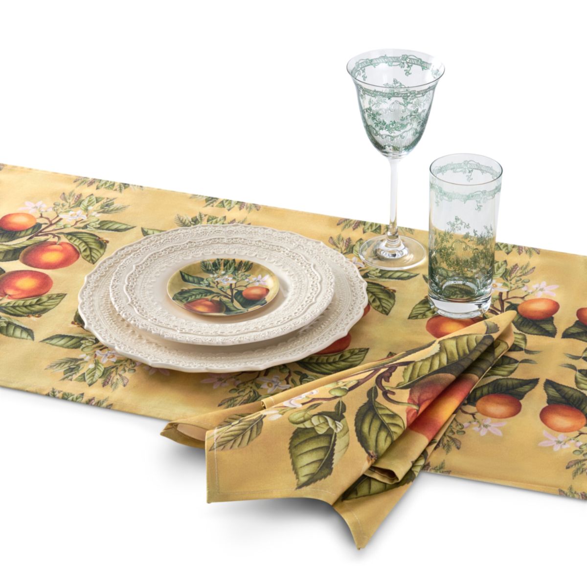 Table setting with a decorative tablecloth featuring fruit patterns, plates, glasses, and napkins.