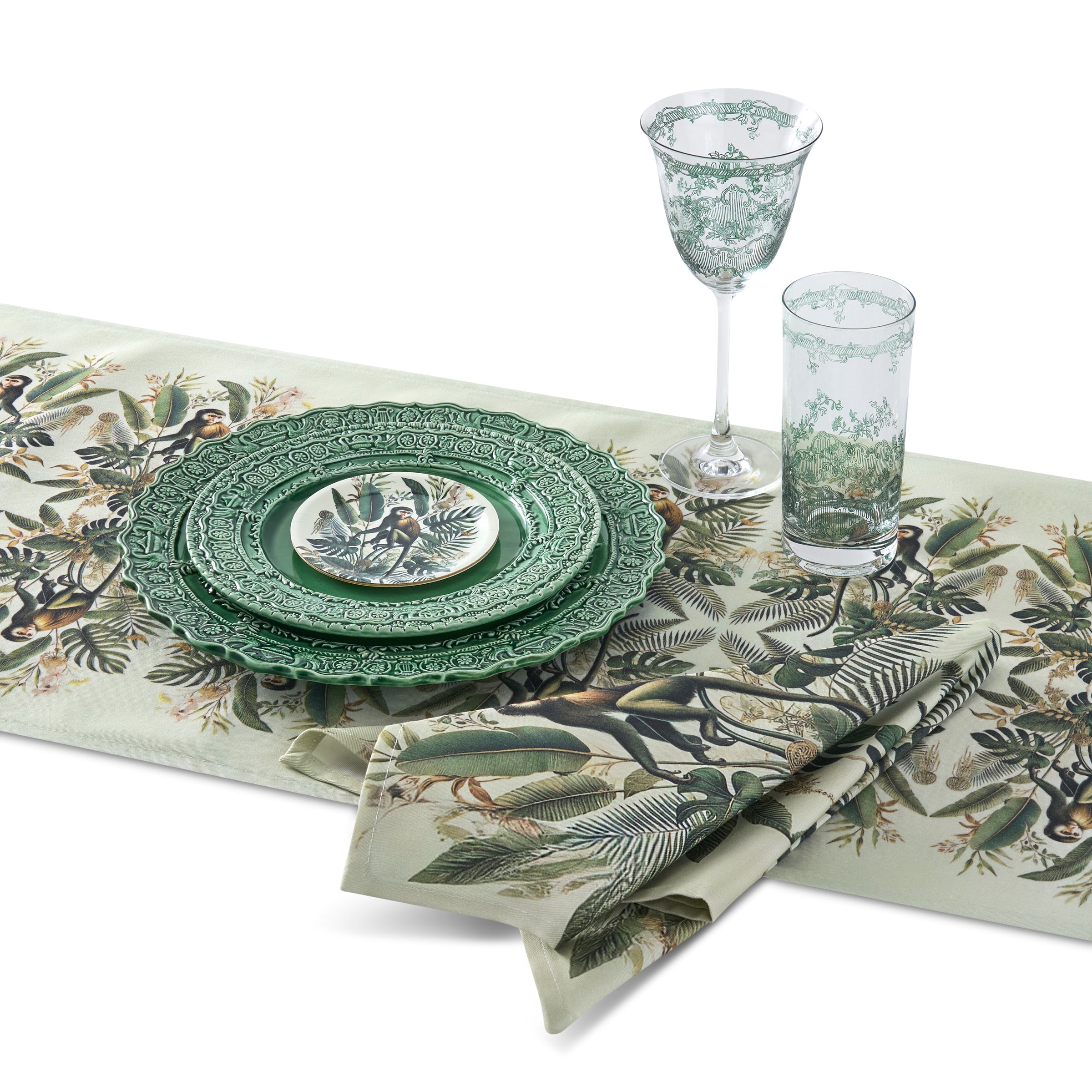 Table setting with green plates, glasses, and napkins featuring animal and plant patterns on a white background.