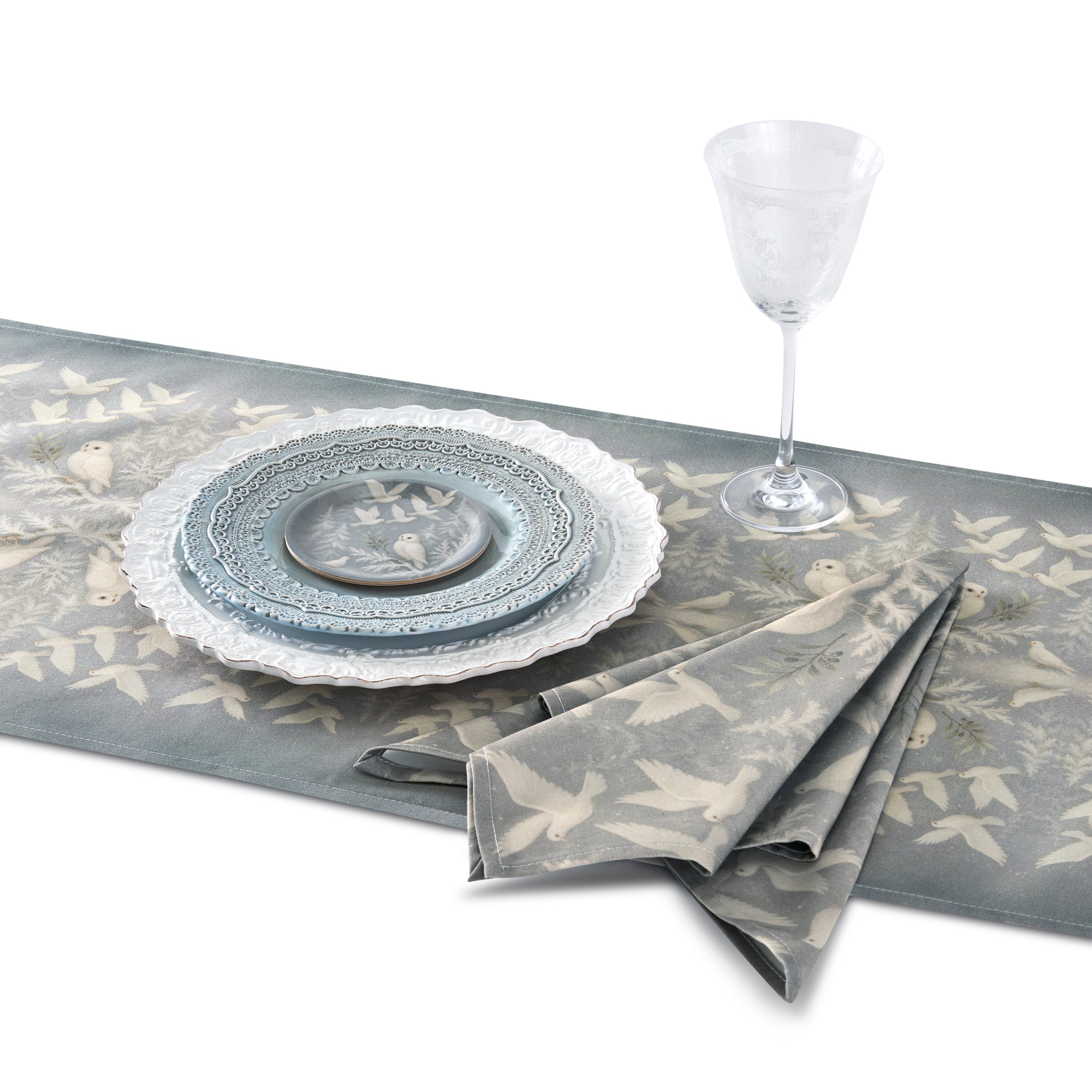 Table setting with gray and white plates, folded napkin, and a glass on a decorative table runner.