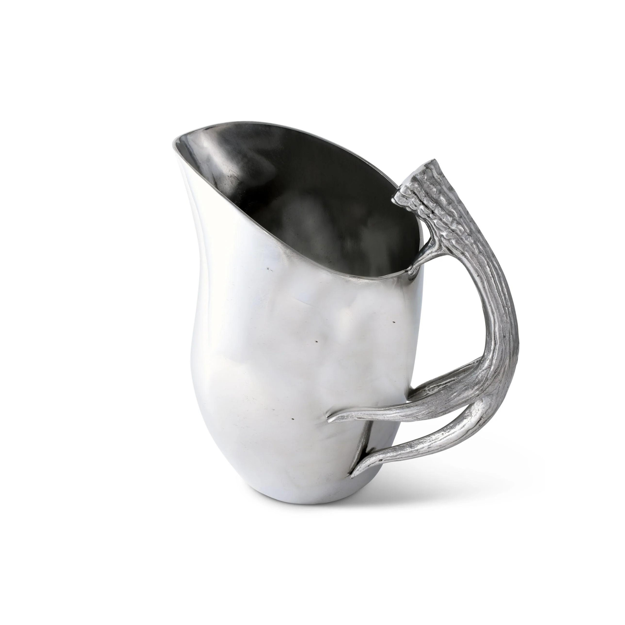 a silver pitcher with an elegantly curved handle resembling a stylized antler. The body of the pitcher is smooth with a reflective surface, and it tapers towards the top, ending in a pointed spout for pouring. The design is modern with organic elements, suggesting a contemporary take on traditional serveware.