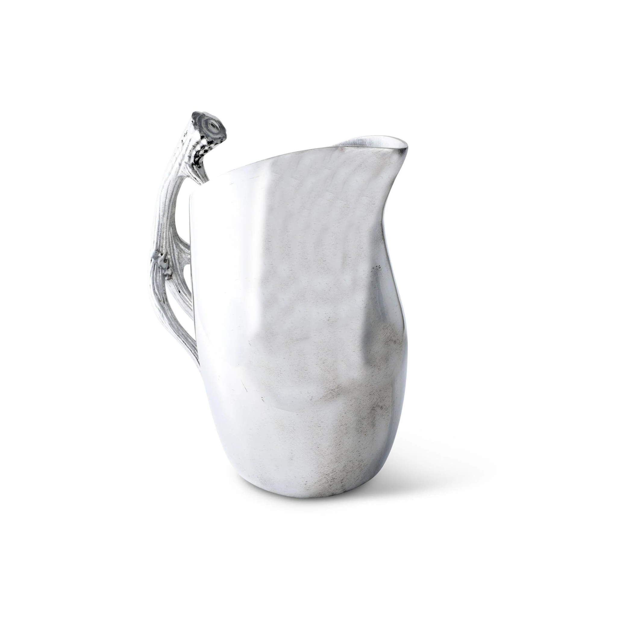 a silver pitcher with an elegantly curved handle resembling a stylized antler. The body of the pitcher is smooth with a reflective surface, and it tapers towards the top, ending in a pointed spout for pouring. The design is modern with organic elements, suggesting a contemporary take on traditional serveware.