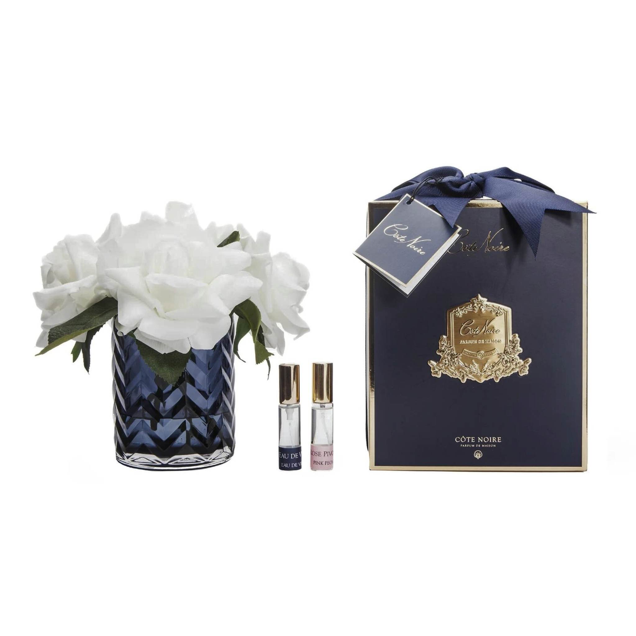 a bottle of fragrance next to a blue herringbone vase with white flowers