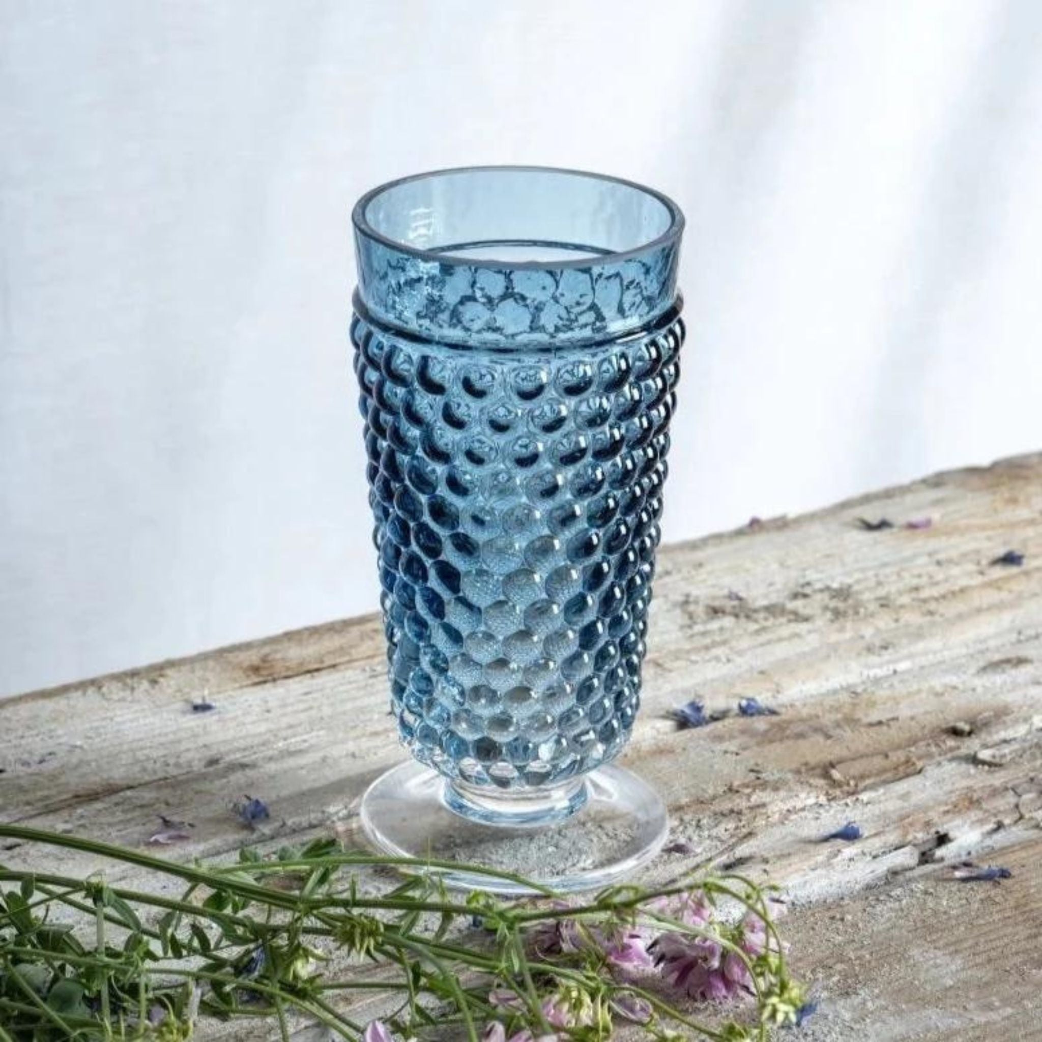 a blue hobnail glass sitting on top of a wooden table