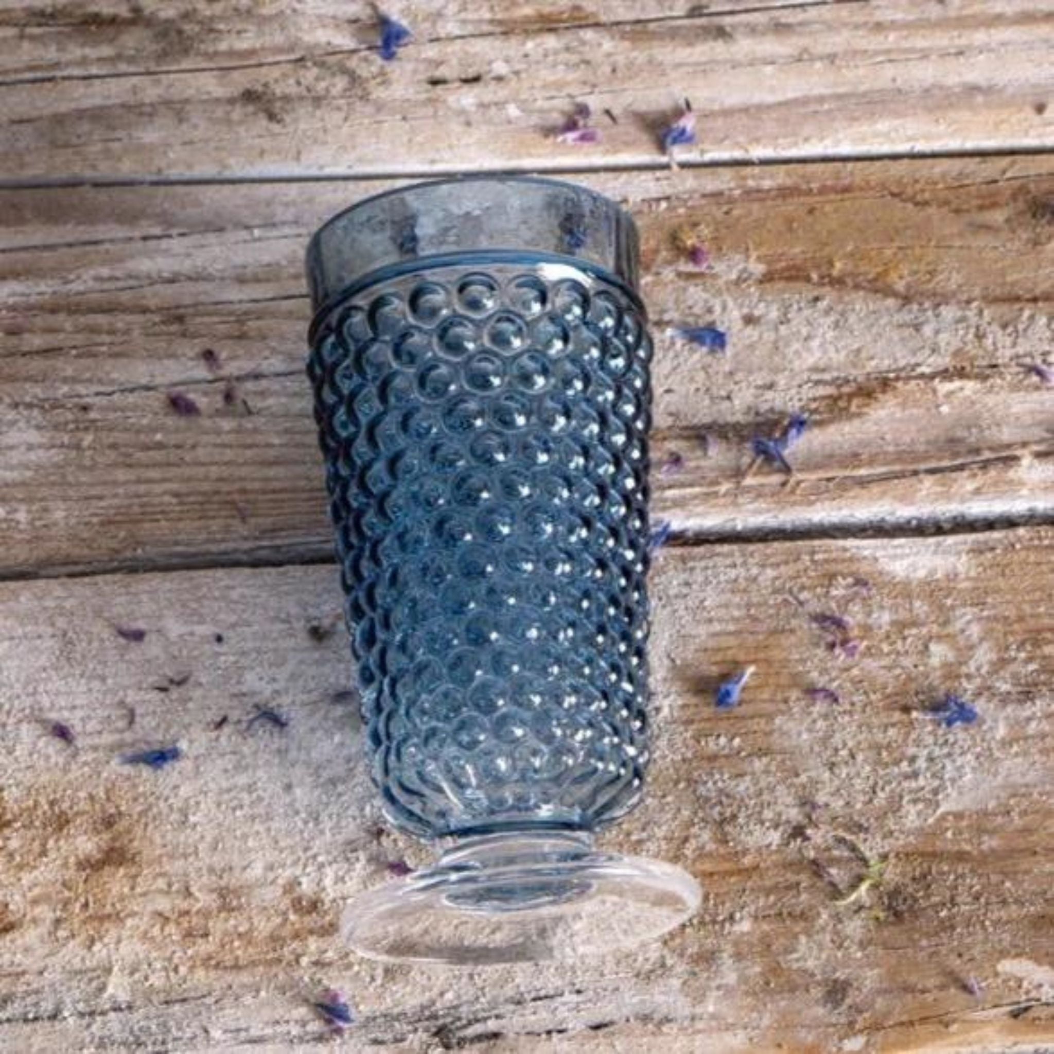 a blue hobnail glass laying on top of a wooden table