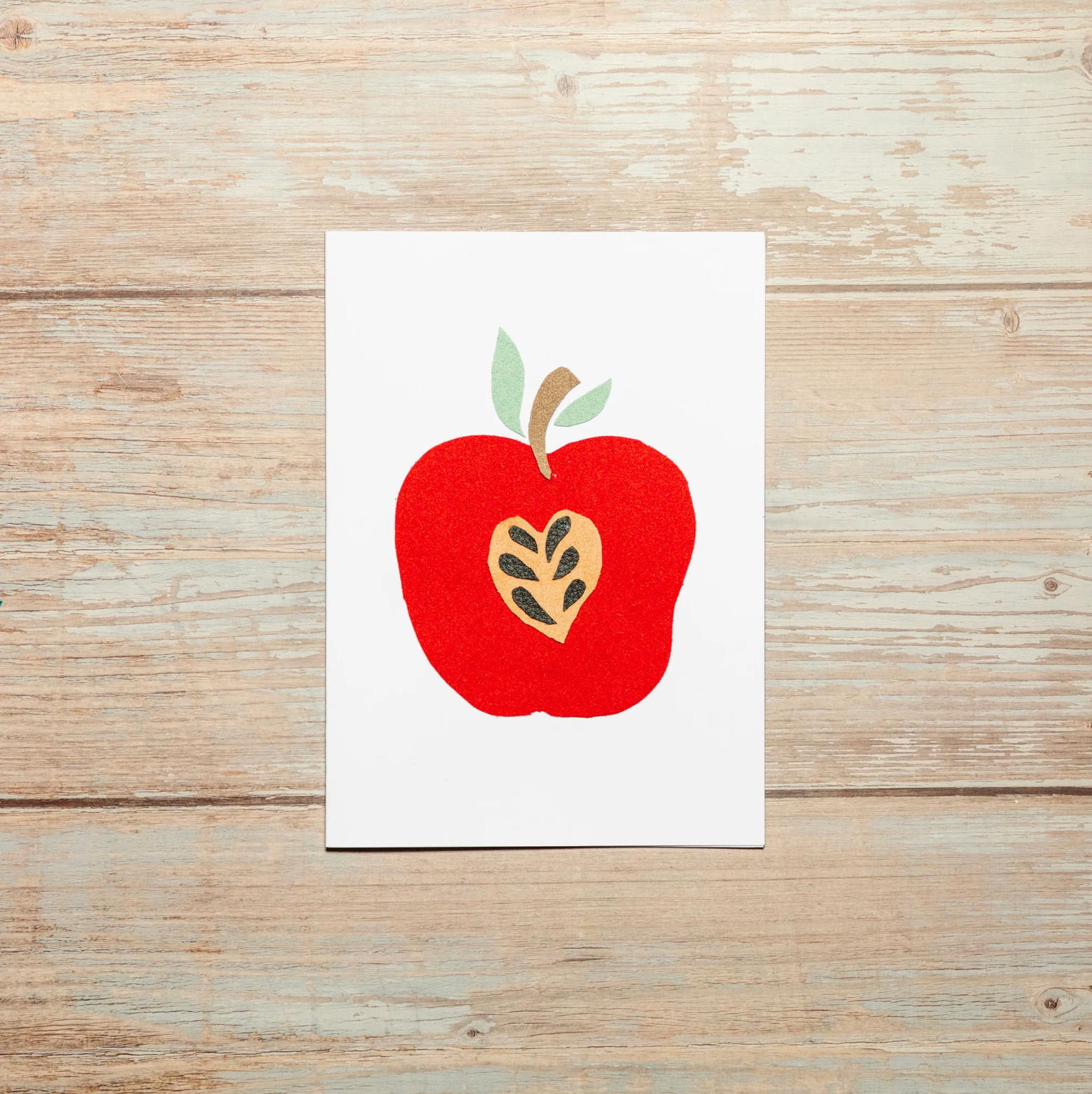 Greeting card with a bright red apple design on a wooden surface