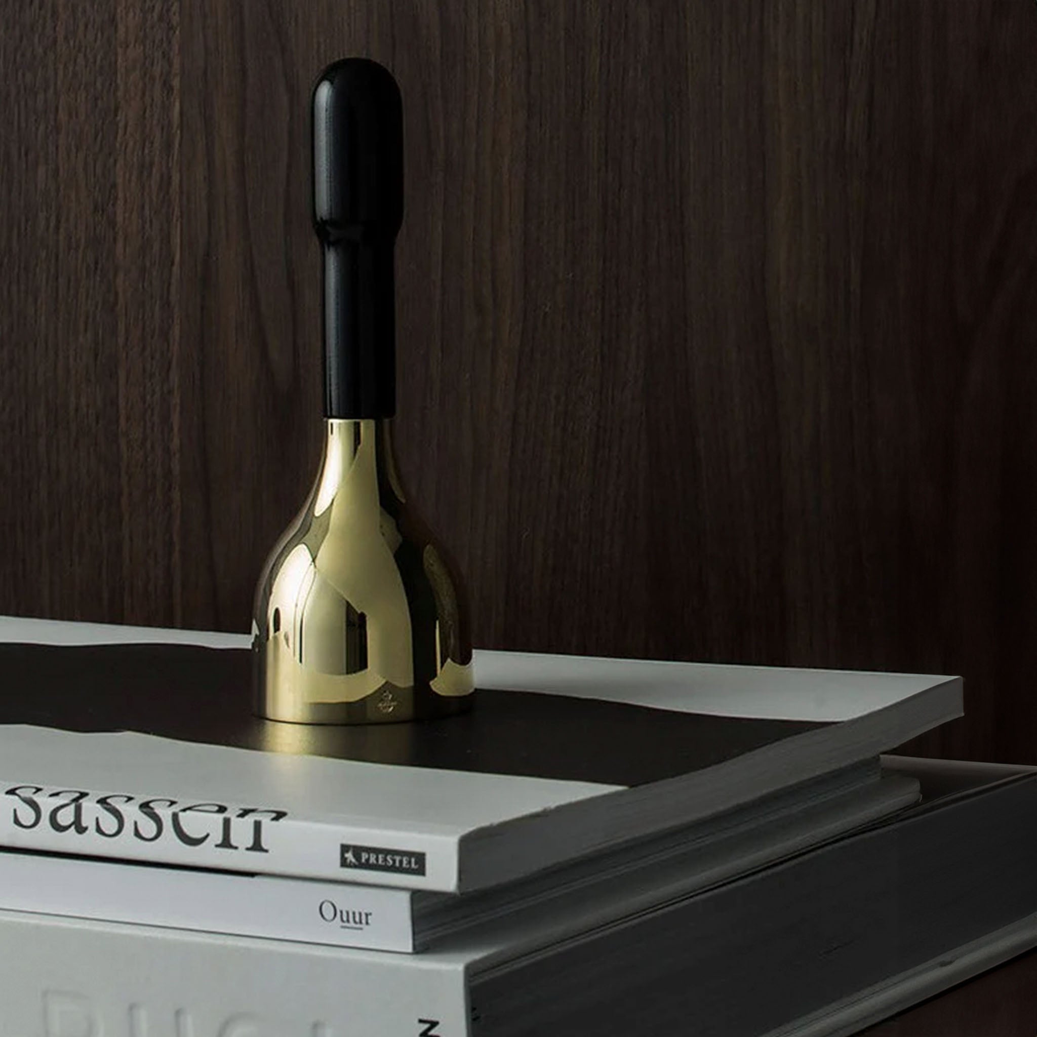 Skultuna Ring My Bell - Black & Brass placed on top of stacked books, styled against a dark wooden background.