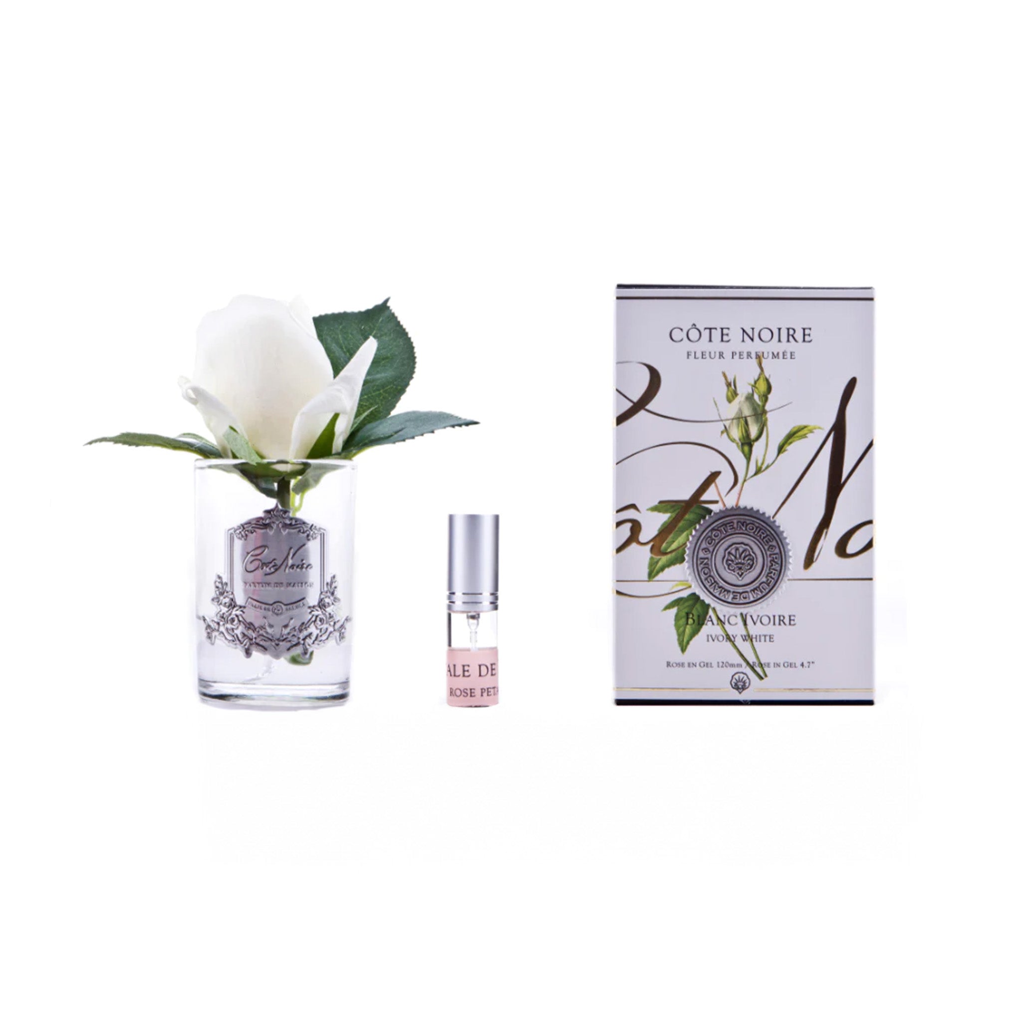 a bottle of fragrance next to an ivory white flower in a clear vase by cote noire