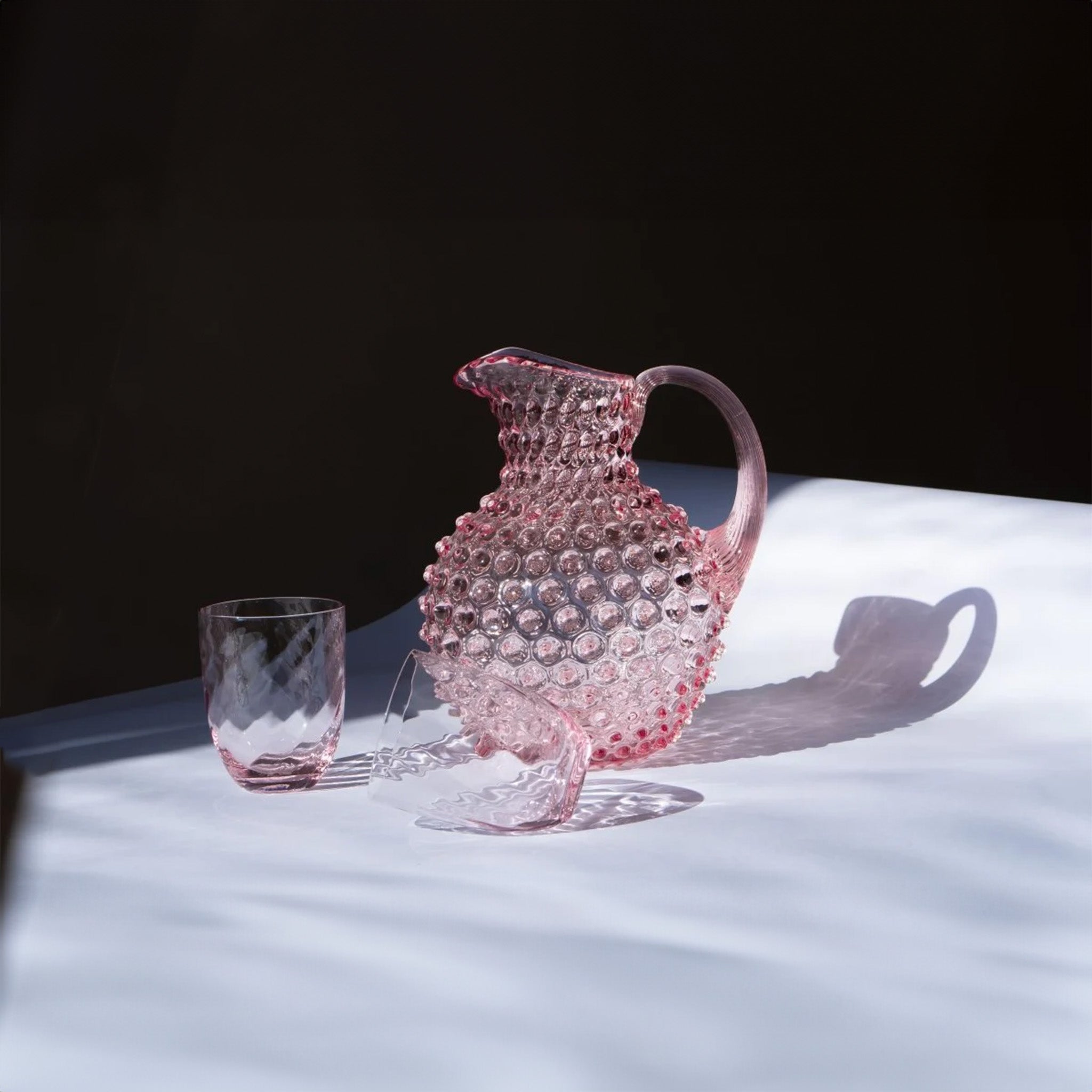 a pink glass pitcher and two glasses on a table