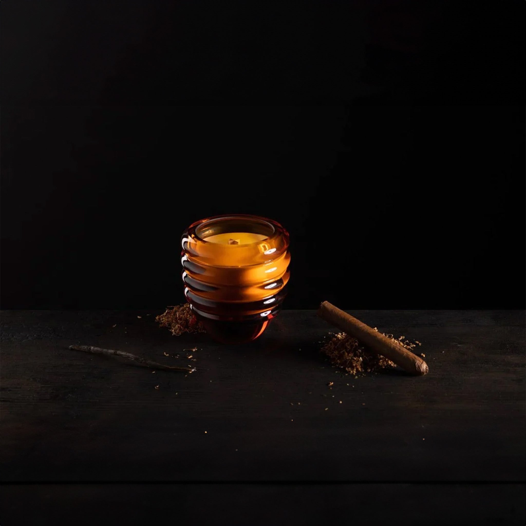 a glass amber candle  sits next to a pile of cinnamon