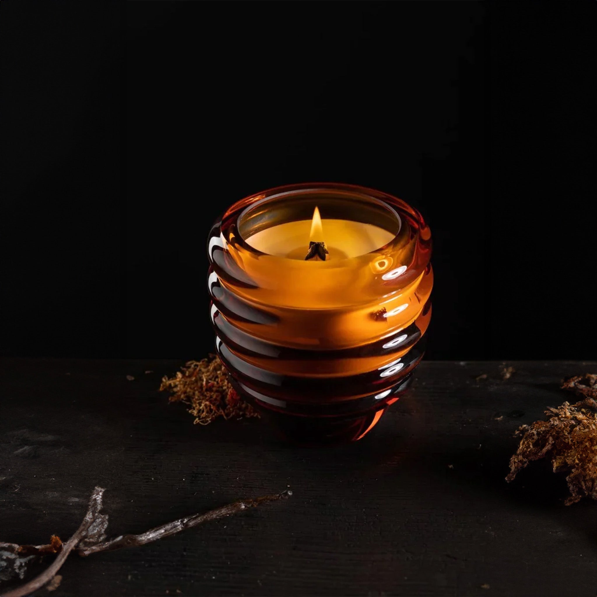 a glass amber candle  that is sitting on a table with vanilla beans on it