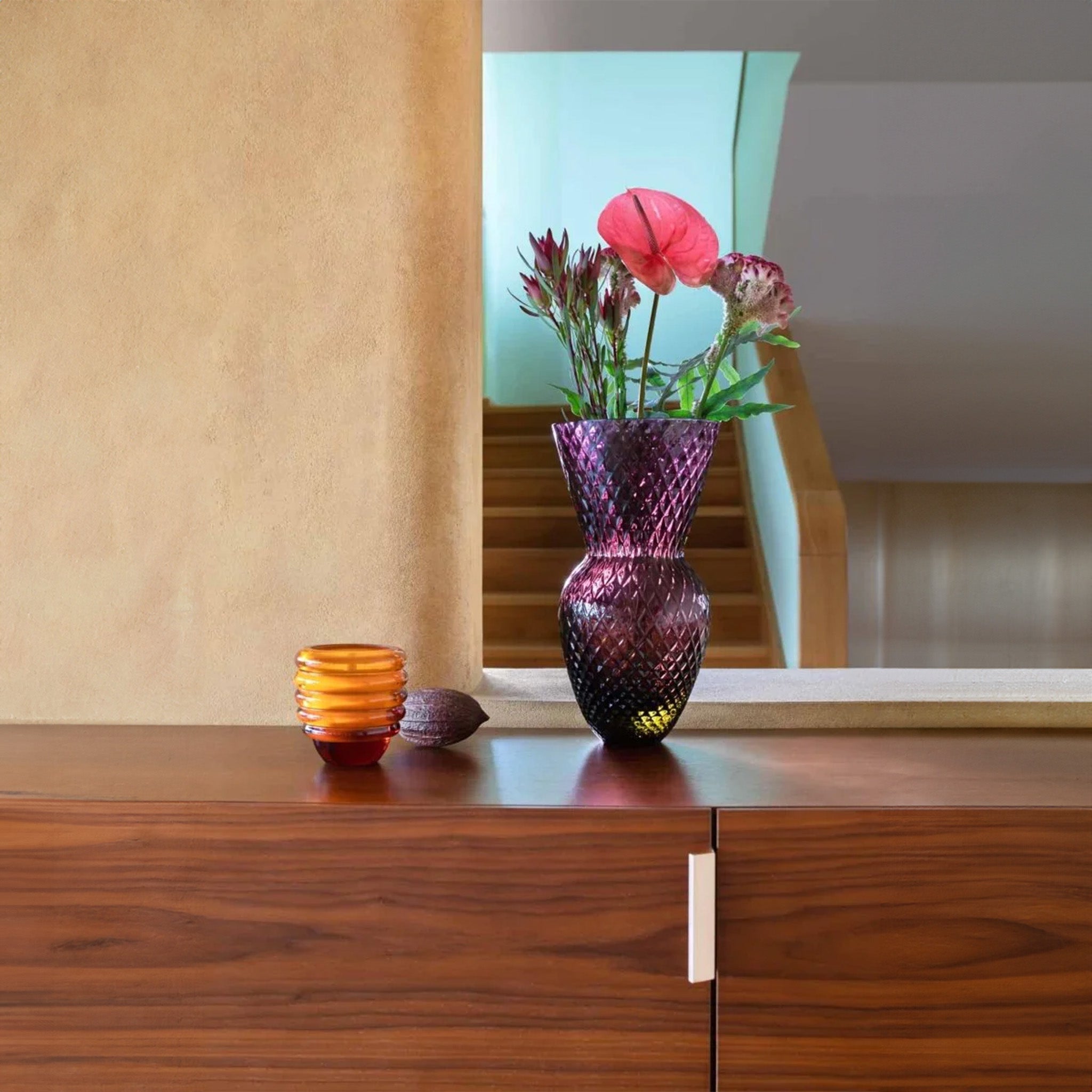 a vase filled with flowers and a glass amber candle sitting on top of a wooden table