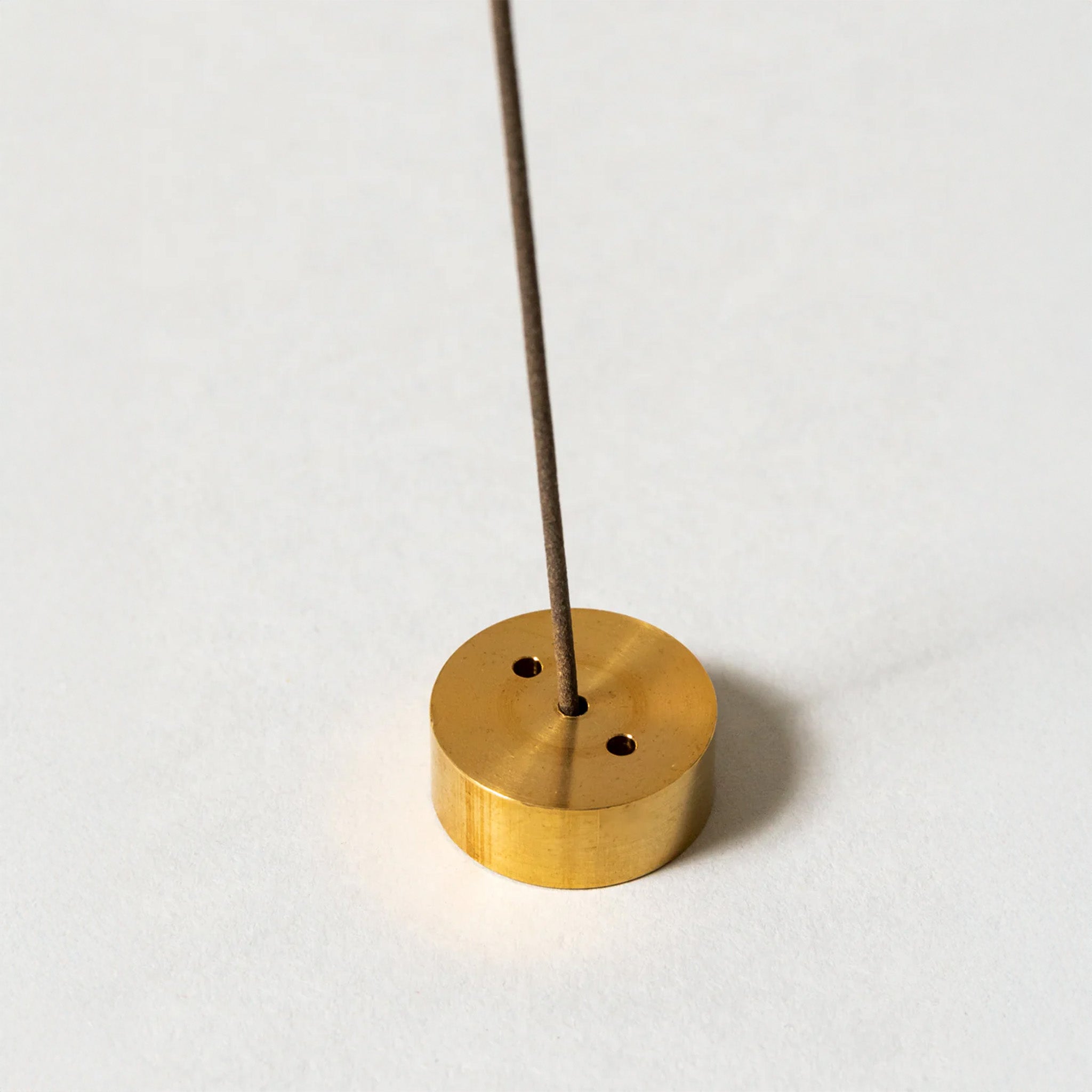 Brass incense holder with an incense stick inserted, showcasing a sleek and simple design on a white background.