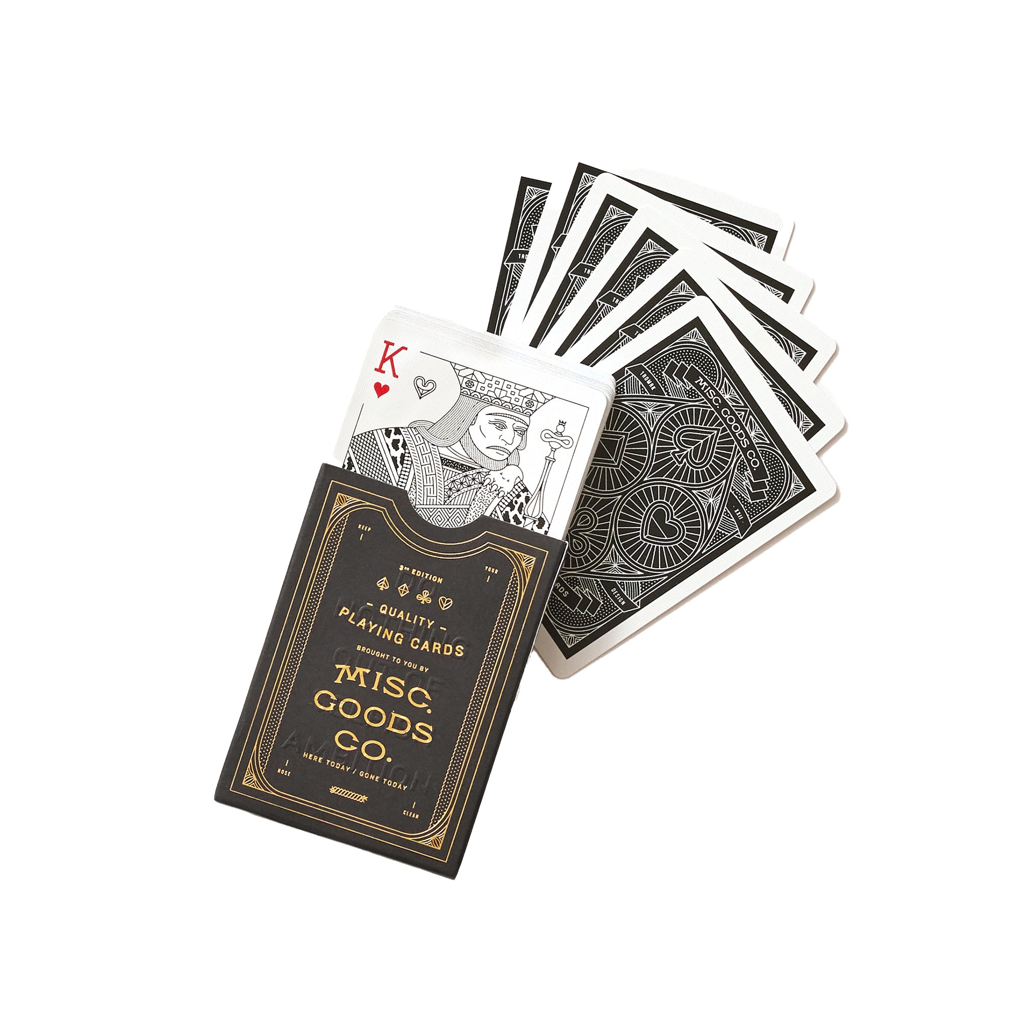 A fan of premium playing cards spread out on a white background, with the King of Hearts card on top displaying a detailed illustration. The back design of the cards is ornate with black and white patterns. The box of the playing cards, with gold and black design, states 'MISC GOODS CO. Quality Playing Cards' and includes the tagline 'They haven't been made, till we make them.' The overall design suggests a luxurious and modern take on the classic deck of cards.