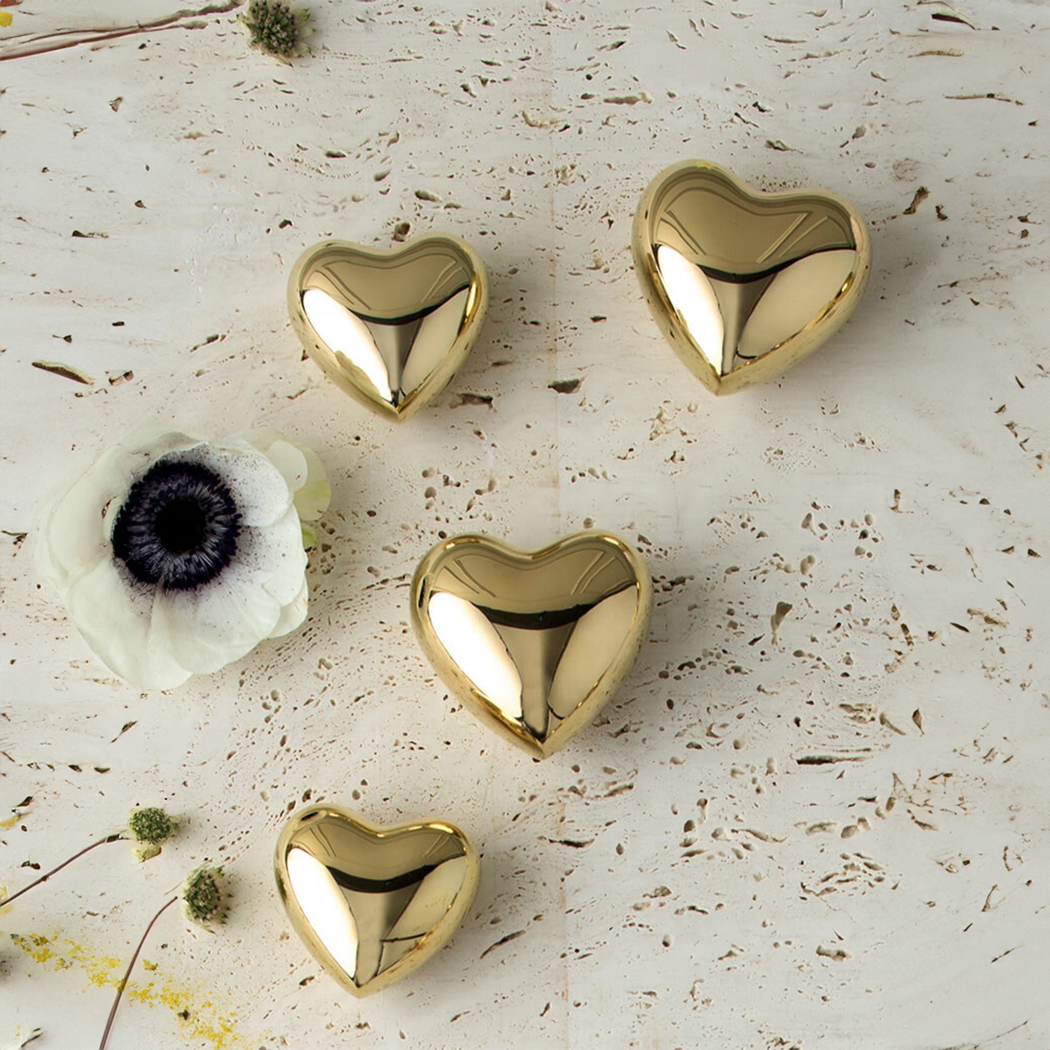 a group of four gold heart paperweights sitting next to a white flower