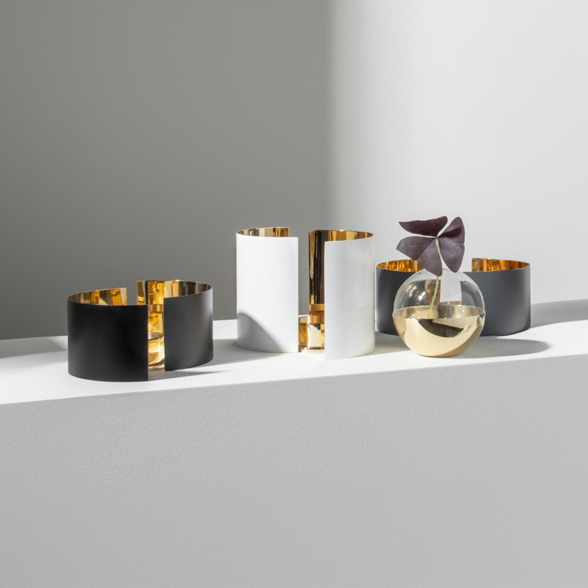 a group of three candle holder by skultuna (black, white, and gray) sitting on top of a white shelf