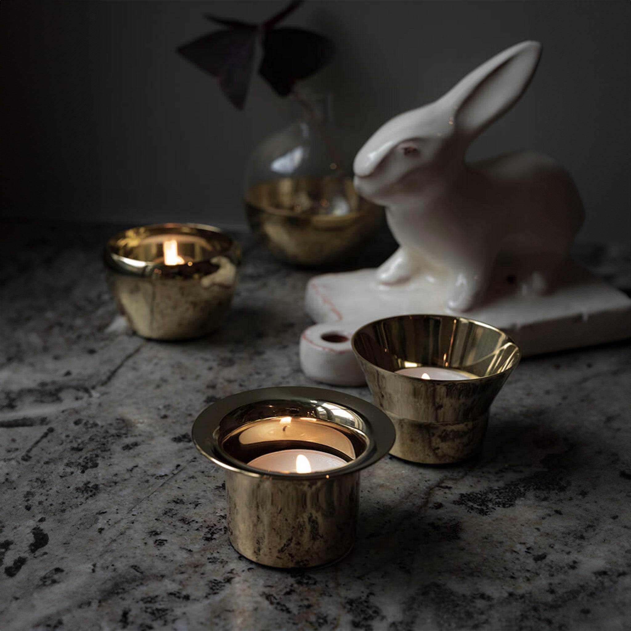 a marble table topped with three brass tealights by skultuna and candles