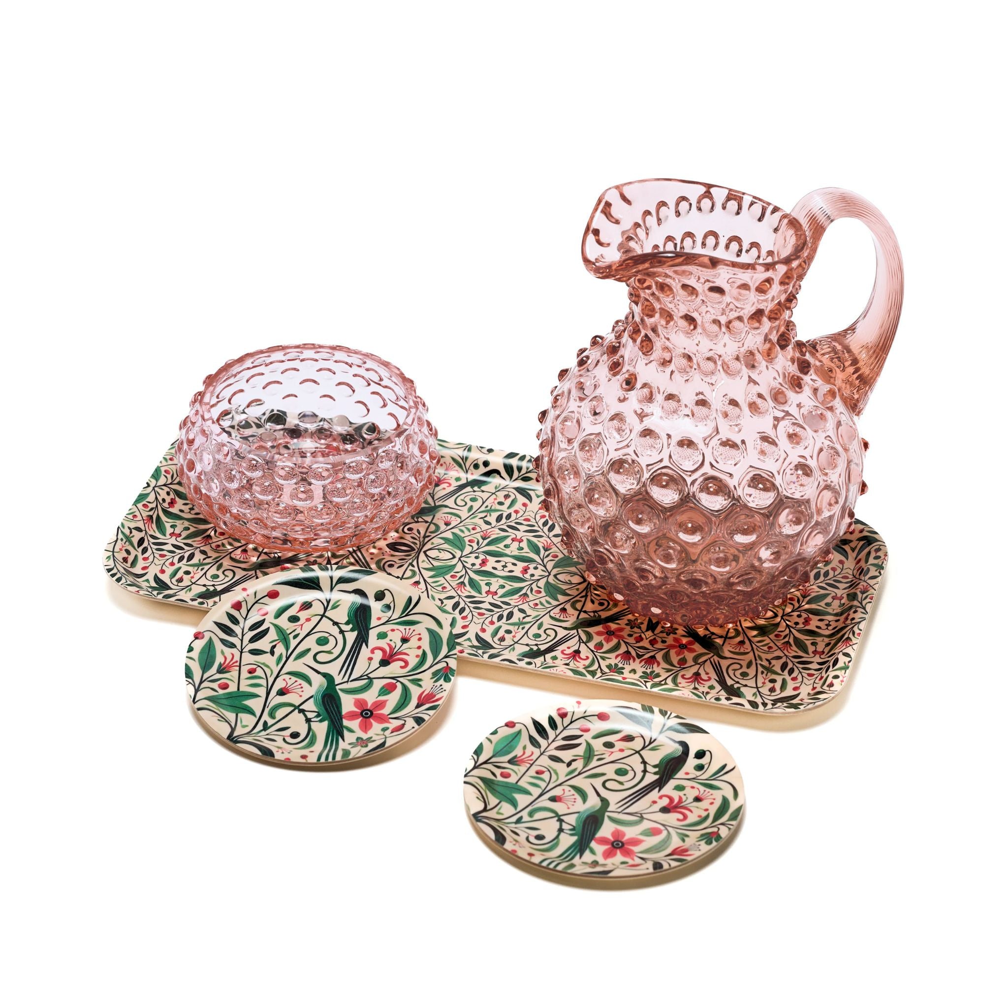 Pink glass pitcher and bowl set with decorative coasters on a white background