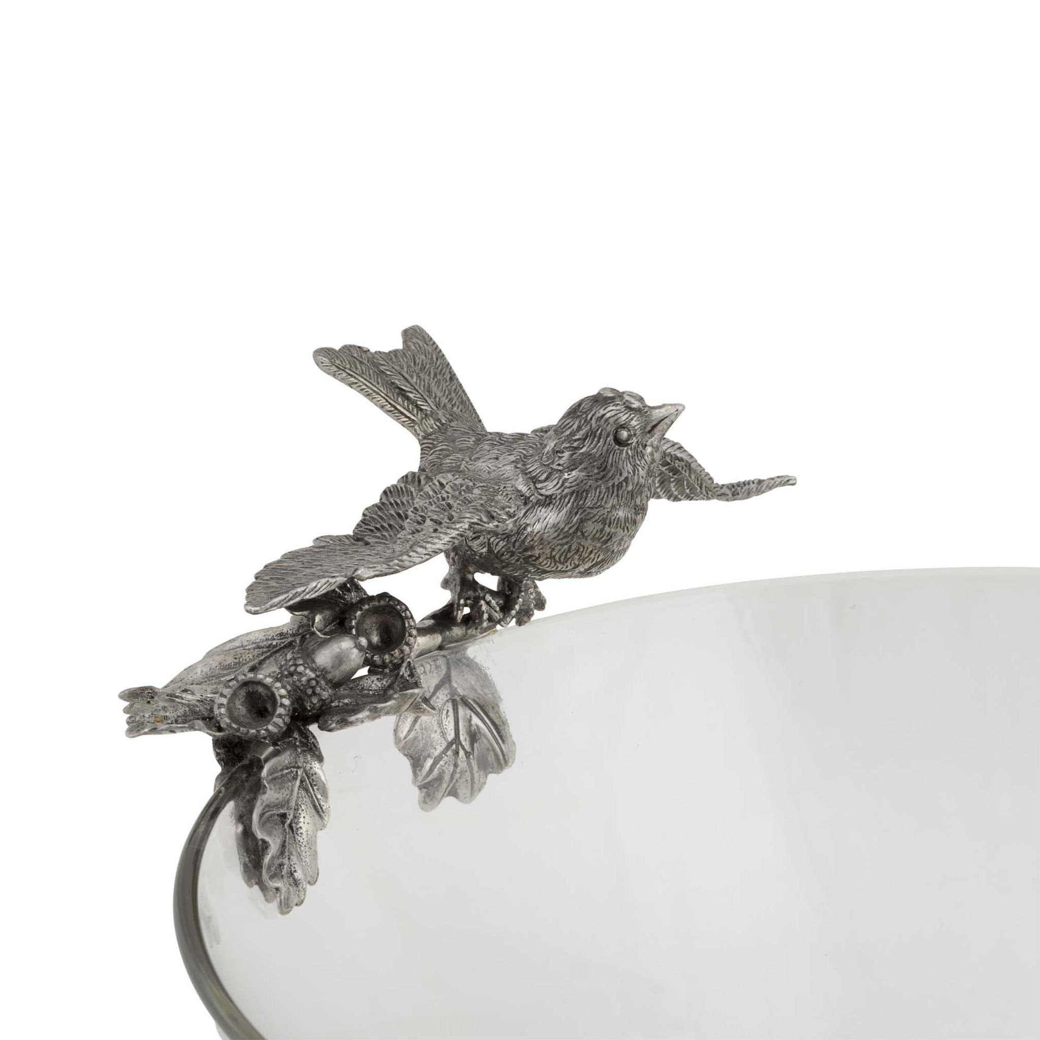 a pewter birds sitting on top of a glass serving bowl